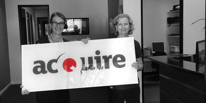 Photo of 2 acQuire staff holding the acQuire company sign